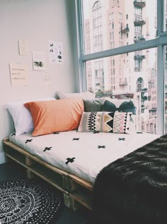 a bed made out of wooden pallets in front of a window with an orange pillow