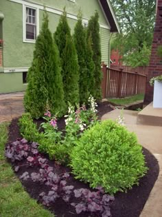 a green house with some bushes and flowers in the front yard