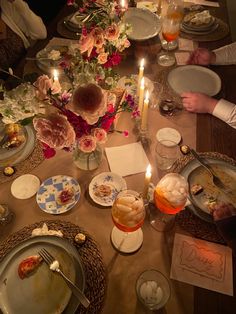 people sitting at a table with plates and candles in front of them, eating food