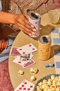 a person sitting at a table with some cards and popcorn on it while holding a drink