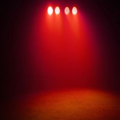 three red spotlights shine brightly on a dark stage with no one in the photo