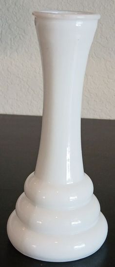 a white vase sitting on top of a black table next to a wall and floor