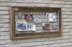 an old wooden frame with pictures hanging on clothes pegs in front of a brick wall