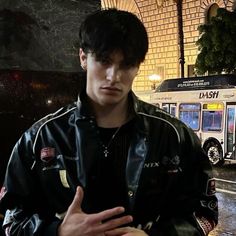 a young man standing in front of a bus on a rainy day with his hands crossed