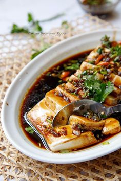 a white bowl filled with tofu and vegetables on top of a woven table cloth