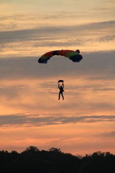 a person is parasailing in the air at sunset or dawn with trees and clouds