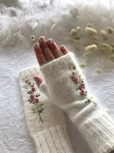 a woman's hand wearing white knitted gloves with flowers on the wrist and fingers