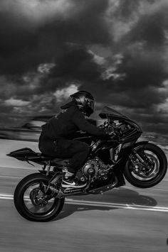 a man riding on the back of a motorcycle down a road under a cloudy sky