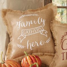 some pumpkins are sitting on a table next to two burluck pillows with the words, family gathers here