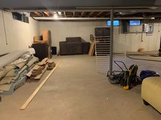 an unfinished basement with various items and tools on the floor, including mattresses and other furniture