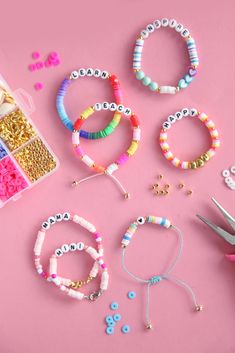 several bracelets, beads and scissors on a pink surface with crafting supplies nearby