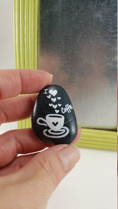 a hand holding a black rock with white writing on it and a green frame in the background