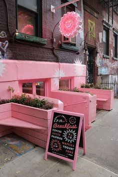 pink benches are lined up on the sidewalk in front of a building with flowers growing out of them