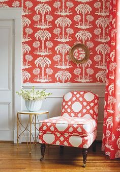 a red chair sitting in front of a window next to a white vase with flowers