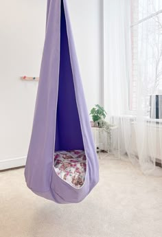 a purple hanging chair in the corner of a room with white walls and carpeted flooring