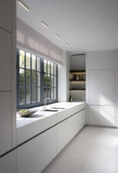 an empty kitchen with white cabinets and counter tops, along with windows that look out onto the trees