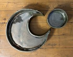 two metal bowls sitting on top of a wooden floor next to each other with one bowl in the shape of a crescent