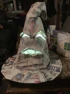 a sculpture made out of newspaper with lights on it's face and mouth, sitting on top of a wooden table