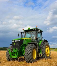 a green tractor is parked in the middle of a wheat field on a cloudy day