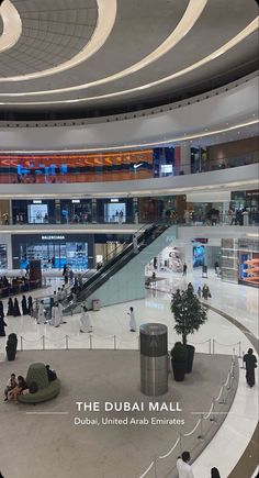 the inside of an airport with people walking and sitting on benches in front of escalators