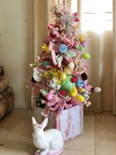 a small white rabbit sitting next to a pink christmas tree with stuffed animals on it