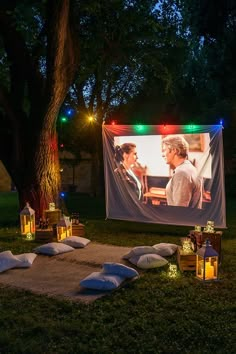 an outdoor movie screen is set up with pillows and candles on the grass in front of it