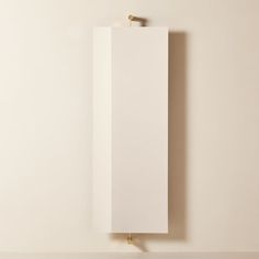 an empty white cabinet hanging on the wall next to a light fixture with a gold hook