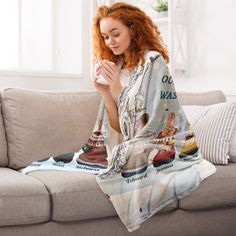 a woman sitting on a couch holding a coffee cup and wearing a blanket with her feet up