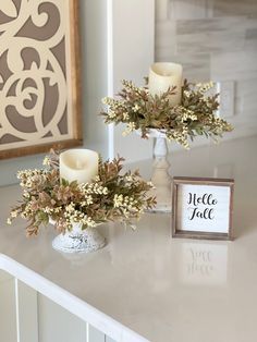 two vases filled with flowers on top of a table next to a framed sign