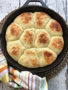 a cast iron skillet filled with bread on top of a white wooden table next to a striped napkin