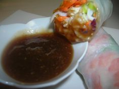 a plate with some food on it and sauce in the bowl next to one roll