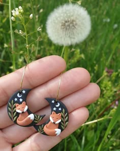 a hand holding a pair of earrings with an animal on the moon and stars painted on it