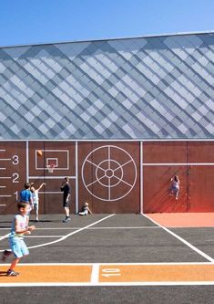 people playing basketball on an outdoor court in front of a large building with geometric designs