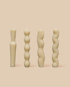 three candles are lined up next to each other in different shapes and sizes on a beige background