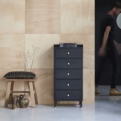 a black dresser sitting next to a wooden wall with a man in the background walking past it