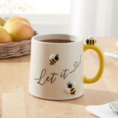 a coffee mug with bees on it sitting next to some pears and apples in the background