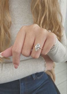 a woman's hand with a diamond ring on her finger, sitting in front of a white sweater