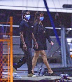 a man and woman walking down the street wearing face masks