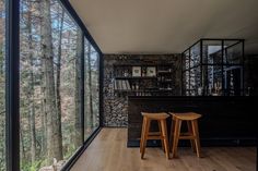 two wooden stools sit in front of a bar with glass walls that overlook the forest