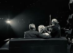 black and white photograph of three people sitting on a bench in front of a stage