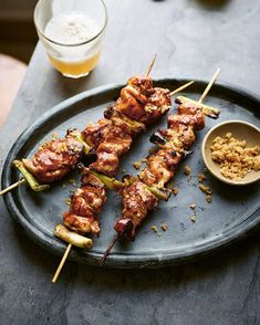 several skewers of meat and vegetables on a plate next to a glass of beer