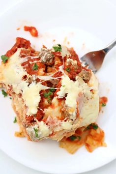 a white plate topped with lasagna covered in sauce and cheese next to a fork