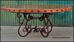 a round table with metal legs and an iron frame on the top, sitting in front of a green painted wall