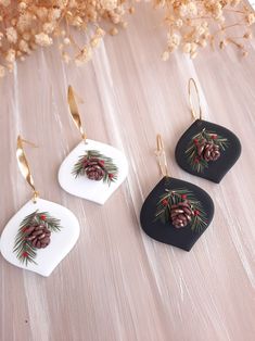 three ceramic ornaments with pine cones and berries hanging from gold - colored earwires