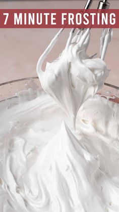 a glass bowl filled with white frosting next to a whisk in it