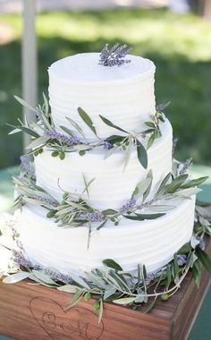 a three tiered white wedding cake with greenery on top