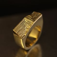 The Xyz Signature ring draws inspiration from modern architecture's Cartesian geometry and mineral structures. To balance against the minimalist solid, Agata hand-carved an intersting pattern on its front that imitates growing crystals forming parallel stritations on the surface. This intricate mineral pattern contrasts beautifully with high-polished surfaces of the ring. Made in 18k gold, this heavyweight ring stands out with its modernist and dynamic aesthetics. Despite its blocky and slightly brutalist appeal, the Xyz Signature ring seamlessly compliments the palm. Ideal future heirloom for mineral and architecture enthusiasts. Please note this ring is handmade and unique, so its texture may vary slightly from the one presented. Finer details: Material: 18k yellow gold. Measurements: 2. Growing Crystals, Signature Ring, Unique Mens Rings, Signature Rings, Ring Stand, The Minimalist, Men's Rings, Modern Aesthetics, Bosnia And Herzegovina