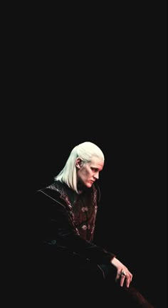 a man with white hair sitting in the dark