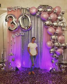 a man standing in front of a purple and silver backdrop with balloons on the wall