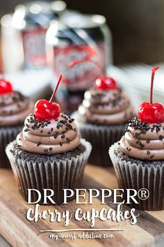 four cupcakes with chocolate frosting and cherries on top are sitting on a cutting board